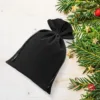 Sacchetti in velluto nero per regali natalizi con rami di pino decorativi.
